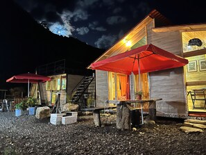 A rustic wooden building with a staircase, outdoor seating with red umbrellas, and a sign reading 'BUHO CAMPS/RE'.