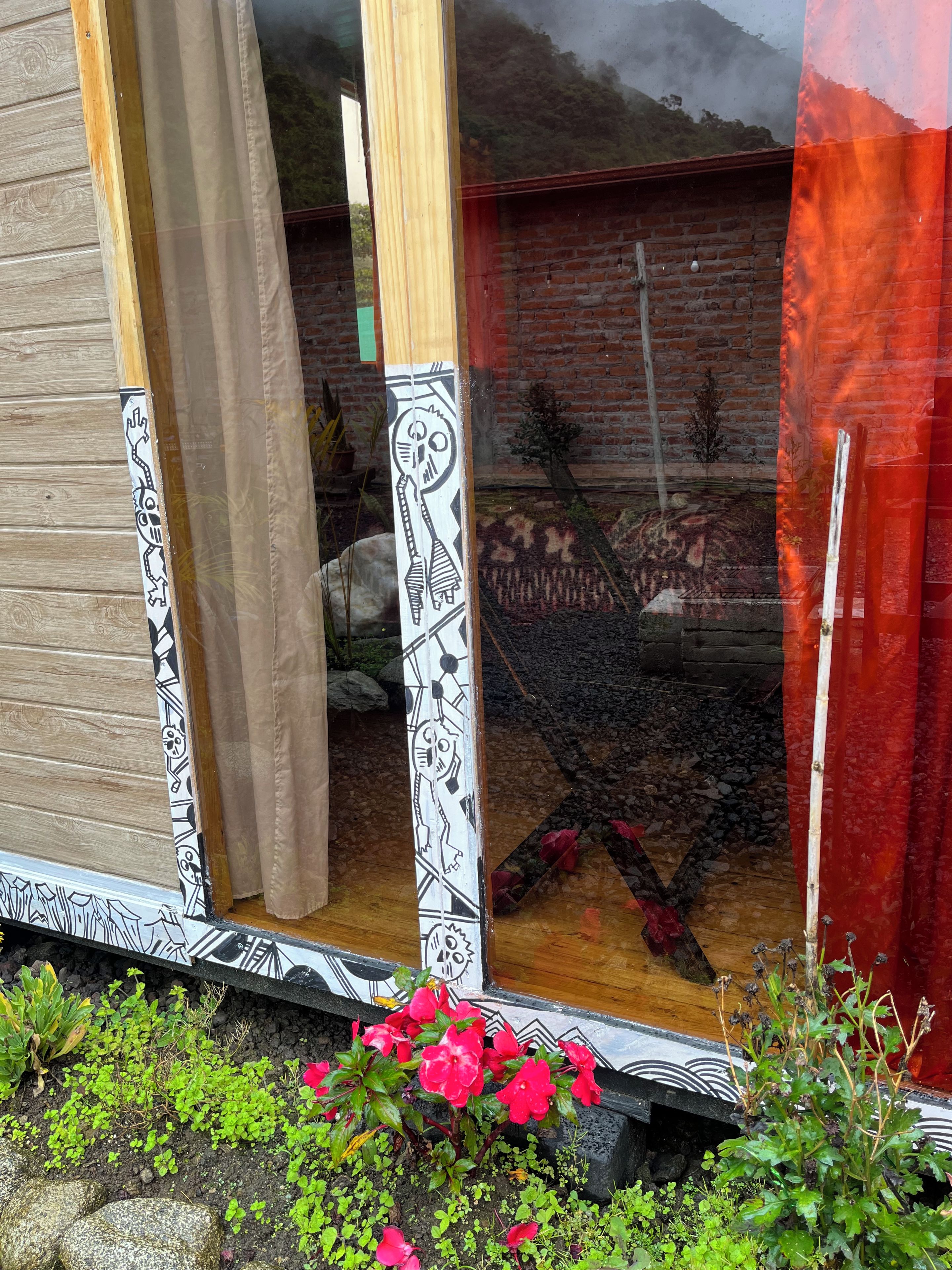 Une fenêtre donnant sur un mur de briques et un jardin où poussent des fleurs rouges.