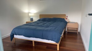 A neatly made bed with a blue comforter and white sheets, a bedside lamp, and a small wooden nightstand with a lamp. - Nature's Gate - Cottage (Newhaven)