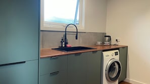 A compact kitchen with a sink, coffee maker, and a washing machine. - Nature's Gate - Cottage (Newhaven)