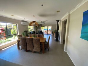 A spacious dining area with a large table and wicker chairs, a ceiling fan, and a view of the outdoors through large windows. - Torquay 3 Bedroom Coastal Retreat (Torquay)