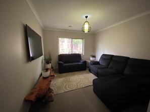 A living room with a flat-screen TV, two black sofas, a patterned rug, and a ceiling light fixture. - Torquay 3 Bedroom Coastal Retreat (Torquay)