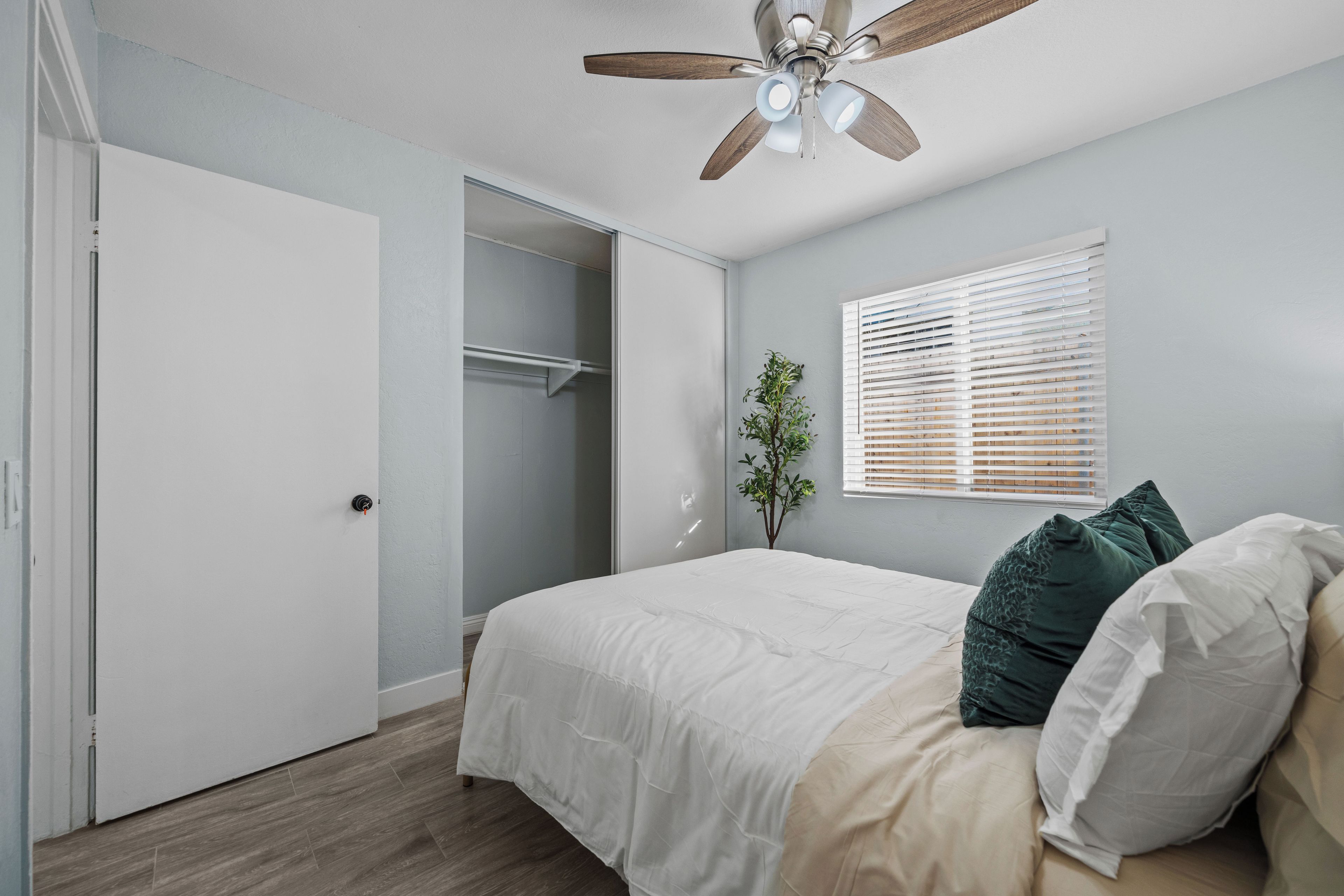 Ein Schlafzimmer mit einem Bett, einem Deckenventilator, einem Fenster mit Jalousien und einem Kleiderschrank.