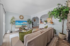Ein Wohnzimmer mit einer Couch, Fernseher, Zimmerpflanzen und Blick auf den Strand.