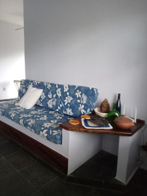 Ein Zimmer mit einem blauen Blumensofa, einem kleinen Holztisch mit Dekoration und einer weißen Wand.