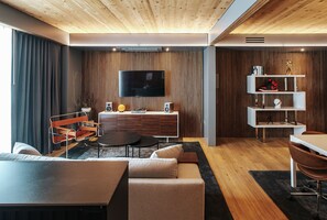 A modern living room with a flat-screen TV, wooden panel walls, a sofa, a coffee table, and a dining area with a table and chairs. - Boutique King Suite with Private Kitchen in East Austin - The Startup (Austin)