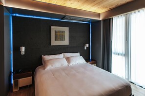 A modern hotel room with a large bed, a dark textured wall, and a ceiling with wooden beams. - Boutique King Suite with Private Kitchen in East Austin - The Startup (Austin)