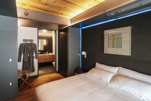 A modern bedroom with a large bed, a wooden ceiling, a dark wall with a decorative mirror, and a visible bathroom. - Boutique King Suite with Private Kitchen in East Austin - The Startup (Austin)