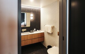 A modern bathroom with a wooden vanity, a large mirror, and a towel hanging on the wall. - Boutique King Suite with Private Kitchen in East Austin - The Startup (Austin)