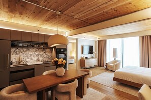 A modern hotel room with a wooden ceiling, a dining area with a wooden table, a bed, and a TV. - (Austin)