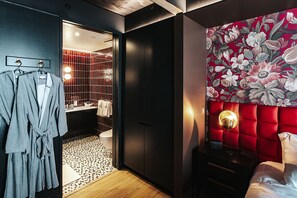 A hotel room with a red upholstered headboard, a wooden floor, a bed with white bedding, a nightstand, and a wall-mounted light fixture. - Boutique King Suite with Private Kitchen in East Austin (Austin)