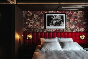 A bedroom with a red upholstered headboard, a framed black and white photograph, and two wall sconces. - Boutique King Suite with Private Kitchen in East Austin (Austin)