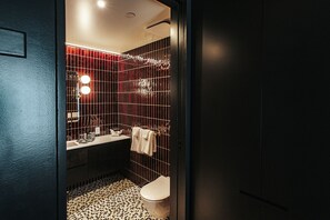 A modern bathroom with a dark color scheme, a tiled floor, a toilet, a sink with a mirror, and a shower area. - Boutique King Suite with Private Kitchen in East Austin (Austin)