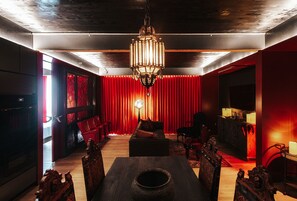 A dimly lit room with a red curtain backdrop, a chandelier, a dining table with chairs, and a television. - Boutique King Suite with Private Kitchen in East Austin (Austin)