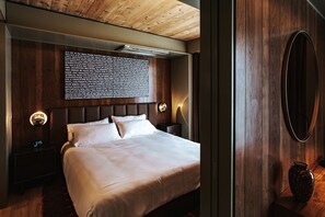 A modern hotel room with a large bed, wooden panel walls, and a wall-mounted light fixture. - Music-Inspired King Suite with Private Kitchen in East Austin (Austin)