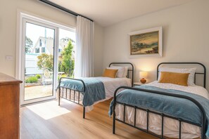 Une chambre avec deux lits, une porte-fenêtre coulissante donnant sur un jardin et un tableau accroché au mur.