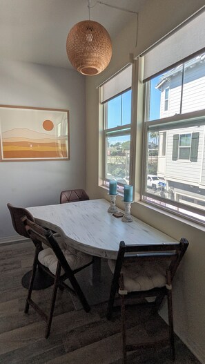 A dining area with a round table, chairs, a hanging light fixture, and a window with a view of the street. - 3-story Serene Surf Loft in perfect Imperial Beach with AC (Imperial Beach)