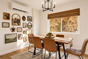 A dining room with a wooden table, leather chairs, a chandelier, and various framed pictures on the wall.