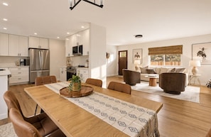 A modern kitchen with white cabinets, stainless steel appliances, and a dining area with a wooden table and leather chairs.