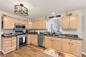 A modern kitchen with wooden cabinets, stainless steel appliances, and a granite countertop. - Cozy Waterview Cottage | Sunroom • Waterfront (Brownsburg)
