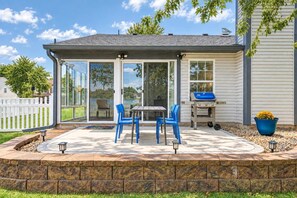 A patio with a table and chairs, a grill, and a potted plant. - Cozy Waterview Cottage | Sunroom • Waterfront (Brownsburg)