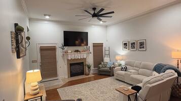 Ein Wohnzimmer mit Kamin, Deckenventilator, Fernseher und einer Couch.