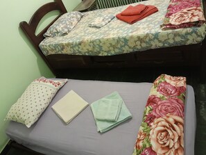 Ein Bett mit blumigem Überwurf, ein gefaltetes rotes Handtuch und zwei Kissen mit verschiedenen Mustern.