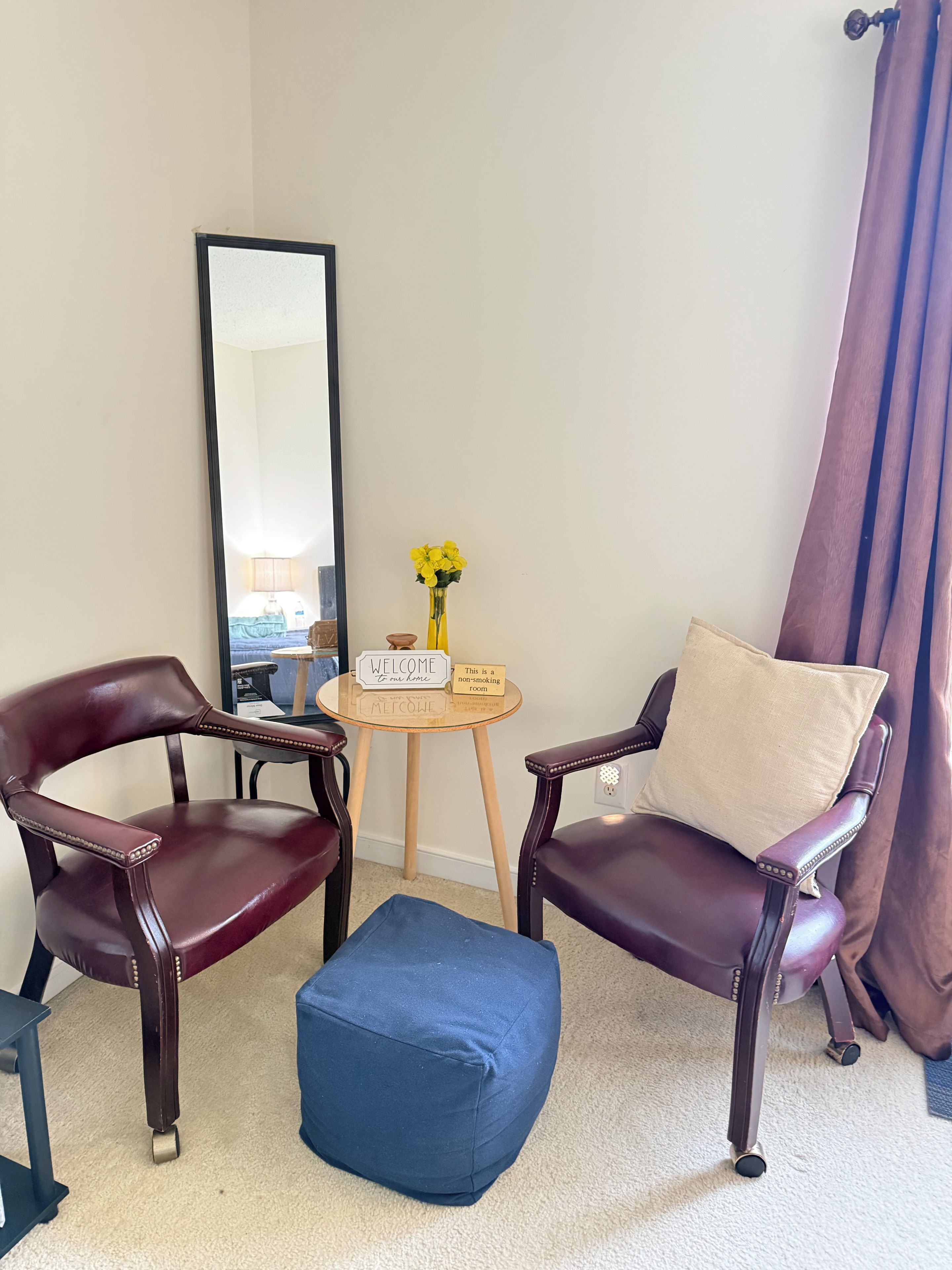 Une pièce comprenant deux fauteuils en cuir, une petite table ronde ornée d’un vase de fleurs jaunes, un miroir et un panneau indiquant qu’il s’agit d’une zone non-fumeur.