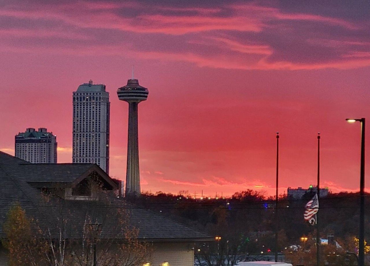 Lo skyline di una città con una torre imponente e un edificio dal design originale, sotto un cielo rosa.