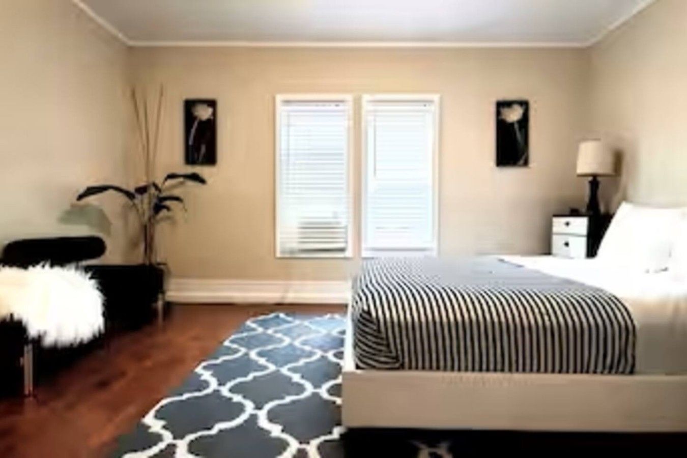 A bedroom with a bed, bedside tables, a lamp, a window with blinds, and a plant.