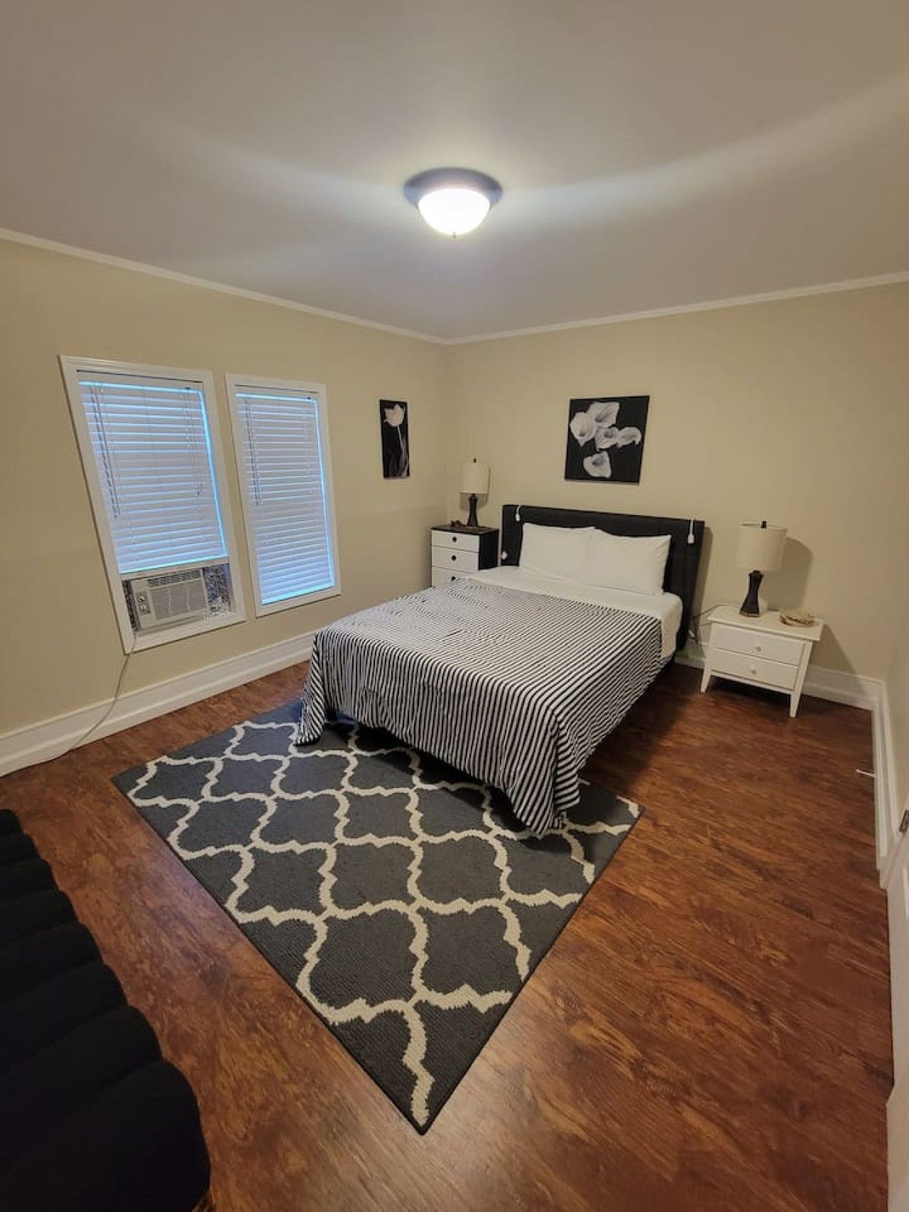 Een slaapkamer met een bed, nachtkastjes, een lamp, en een raam met jaloezieën.