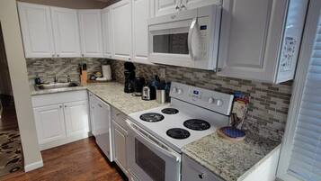 A kitchen with white cabinets, a microwave, a stove, and a trash can.