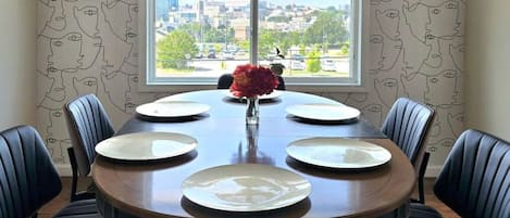 Ein Esszimmer mit einem runden Tisch, gedeckt für sechs Personen, flankiert von sechs Stühlen und einem Fenster mit Blick auf die Stadt.