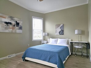 Une chambre à coucher avec un lit, des tables de chevet, une fenêtre et des œuvres d’art accrochées aux murs.