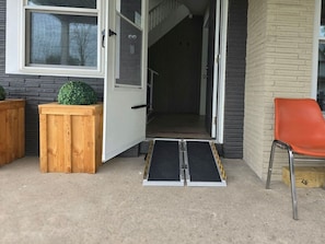 A doorway with a ramp leading into a building, a wooden planter, and an orange chair outside. - “Life is Good” | Accessible Stay Near the Falls (Niagara Falls)