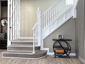 A staircase with white railings and wooden steps, a small table with a picture frame, and a wall with vertical stripes. - “Life is Good” | Accessible Stay Near the Falls (Niagara Falls)