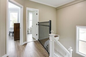 Un couloir doté d’un plancher en bois, d’une porte blanche et d’un portail noir menant à une autre pièce.