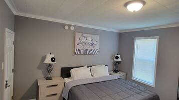 Een slaapkamer met een bed, twee nachtkastjes, een lampje, een raam met zonwering en een plafondlamp.