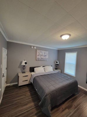 Een slaapkamer met een bed, twee nachtkastjes, een lampje, een raam met zonwering en een plafondlamp.