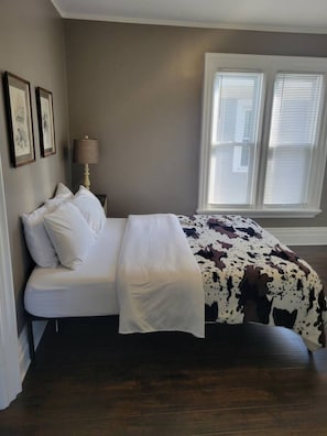 A bedroom with a bed, a nightstand, a lamp, and a window with blinds. - Perfect for Large Groups 10BR Sleeps 26 Near Falls (Niagara Falls)