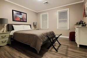 Ein Schlafzimmer mit einem Bett, Nachttischen, einer Lampe, einem Schminktisch und einem Fenster mit Jalousien.
