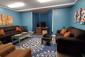 Ein Wohnzimmer mit blauer Wand, einem Flachbildfernseher, einem Couchtisch und zwei Sofas mit Kissen.