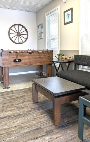 A room with a wooden foosball table, a sofa, and a coffee table. - Gray Goose - Walk to Falls | Spacious 4BR Home (Niagara Falls)