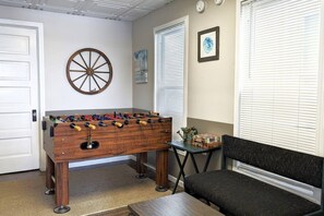 A room with a foosball table, a sofa, and a small table with items on it. - Gray Goose - Walk to Falls | Spacious 4BR Home (Niagara Falls)