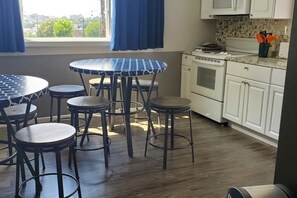 A kitchen with white cabinets, a microwave, and a stove. There is a round table with a patterned tablecloth and four stools. - Gray Goose - Walk to Falls | Spacious 4BR Home (Niagara Falls)