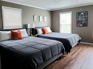A bedroom with two beds, a nightstand, a lamp, and artwork on the wall. - Gray Goose - Walk to Falls | Spacious 4BR Home (Niagara Falls)