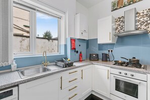A kitchen with white cabinets, a stainless steel sink, a toaster, a kettle, and a stove. - Greater Manchester | Whole home | 5-Bedroom | Sleeps 8 | (Tyldesley)