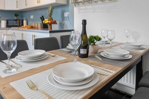 A dining table set for a meal with plates, glasses, cutlery, and a bottle of wine. - Greater Manchester | Whole home | 5-Bedroom | Sleeps 8 | (Tyldesley)