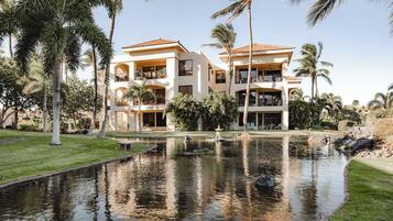A two-story building with balconies, surrounded by palm trees and a pond.