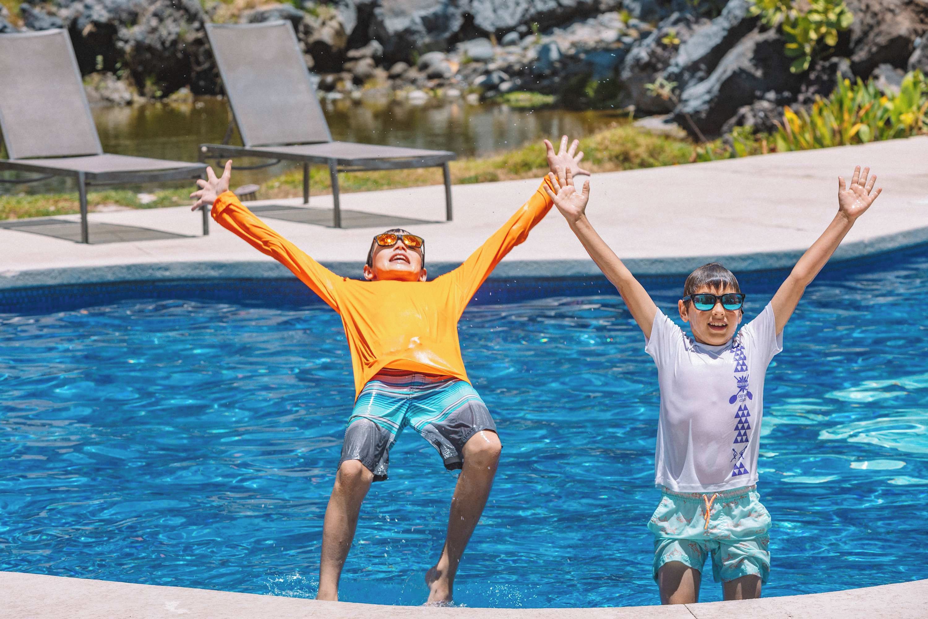 A swimming pool with two people in the water, one wearing an orange shirt and the other in a white shirt.